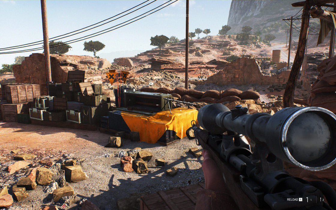 A sniper's perspective in Battlefield V, overlooking a desert outpost filled with supply crates and sandbags, ready for a long-range engagement. Experience realistic WWII combat with an EA Play Origin CD Key from RushGame.co