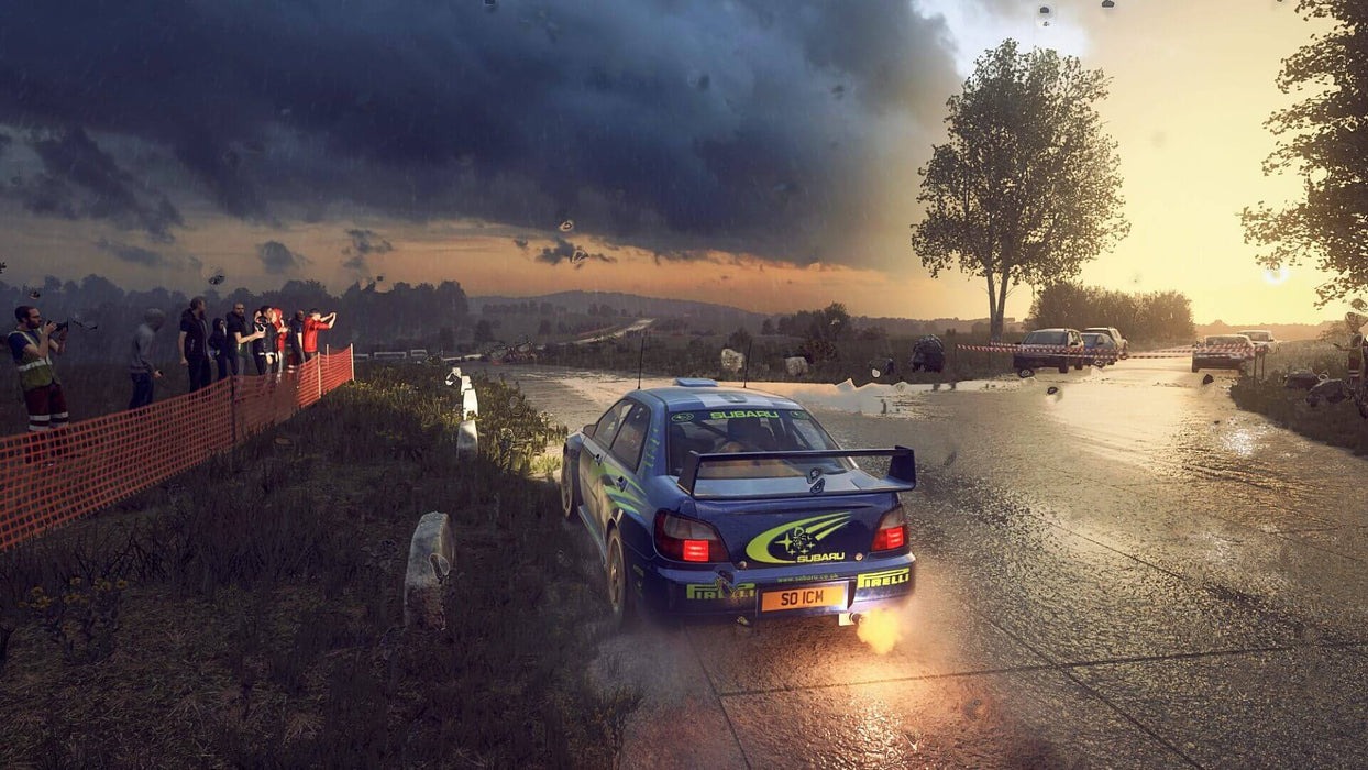 In-game screenshot from DiRT Rally 2.0 showcasing a classic Subaru Impreza WRX rally car racing on a wet and muddy countryside track, with spectators watching from the sidelines. Get your Xbox digital key at RushGame.co