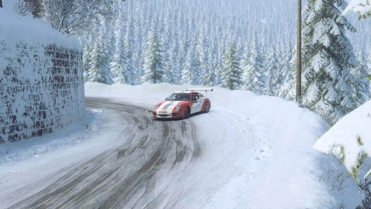 Gameplay screen - Winter rally scene in DiRT Rally 2.0 with a Porsche 911 GT3 navigating a snowy mountain road, showcasing realistic driving physics and weather effects. Purchase your Xbox digital activation key now at RushGame.co