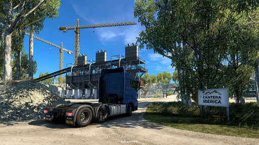 Gameplay screenshot from Euro Truck Simulator 2 - Iberia DLC, featuring a large truck entering a quarry named "Cantera Ibérica." Towering cranes and industrial structures set the backdrop for a realistic transport experience. Buy Euro Truck Simulator 2 - Iberia DLC PC Steam CD Key at RushGame.co and explore the roads of Spain and Portugal