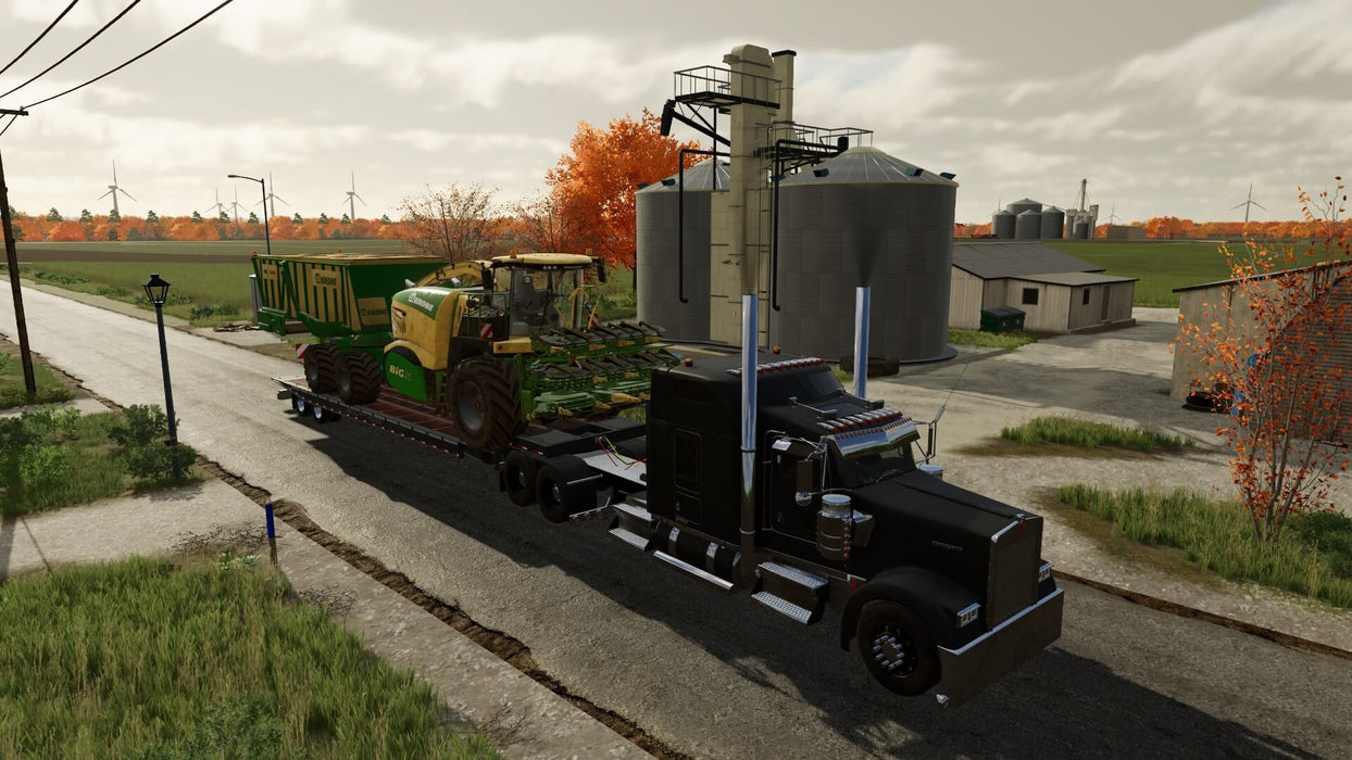 Gameplay screenshot - A black semi-truck hauling a large Krone Big X agricultural machine on a flatbed trailer in Farming Simulator 22: Premium Edition, passing by silos and a farm setting. Build your ultimate farm—get your digital Steam key now at RushGame.co!
