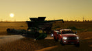 Gameplay screen - A massive harvester with an American flag design and a red pickup truck working together in a golden wheat field at sunset in Farming Simulator 22: Premium Edition. Experience realistic farming with your Steam CD Key from RushGame.co!