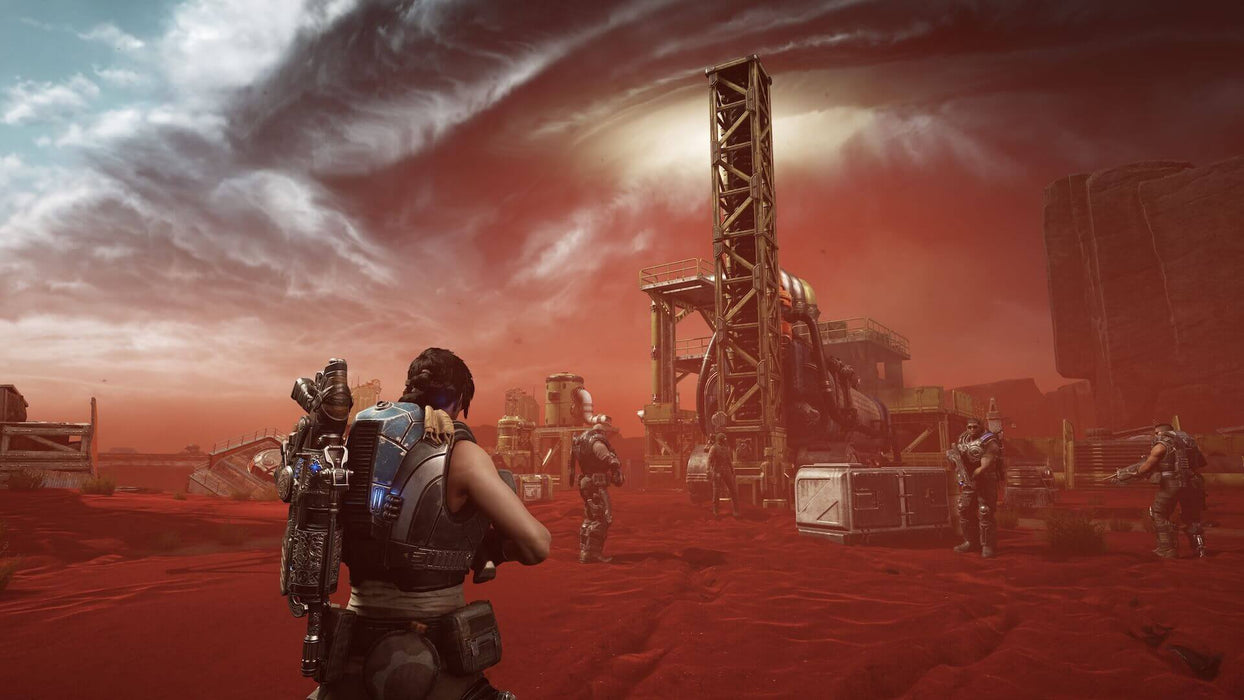 Gameplay screenshot - Kait Diaz leads a squad in a fiery red desert storm, approaching an industrial structure in Gears 5. The apocalyptic setting enhances the immersive combat experience. Purchase your Gears 5 Game of the Year Edition Xbox and PC key at RushGame.co today