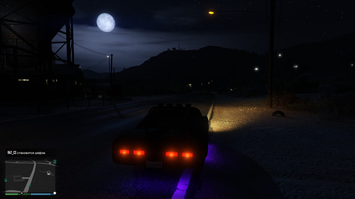 Gameplay screenshot - A black muscle car cruises through the countryside under the moonlit sky in Grand Theft Auto V for Xbox One. Experience immersive night driving and an expansive open world—get your GTA V CD Key at RushGame.co