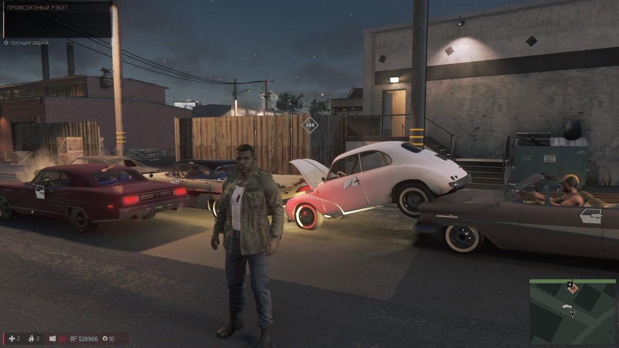 Gameplay scene from Mafia III: Definitive Edition with protagonist Lincoln Clay standing among retro cars in a night-time urban environment. Get the Xbox One/Series X|S digital version today at RushGame.co