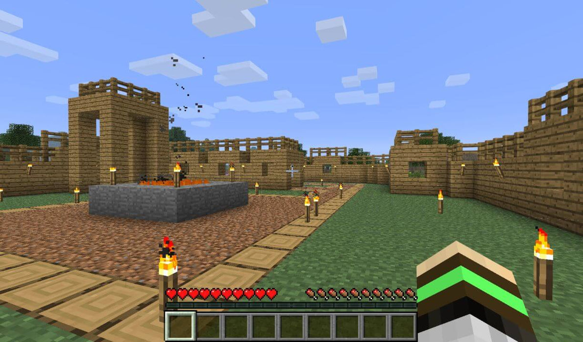 A player stands in a wooden village surrounded by lit torches and a central stone platform in Minecraft Deluxe Collection for Nintendo Switch. Explore the sandbox world and build unique structures. Get your Minecraft game keys at RushGame.co