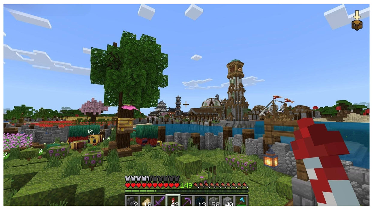 Detailed Minecraft gameplay scene showing a peaceful village with bees, flower gardens, and a large tower across the water. Start your sandbox journey today with a Minecraft Xbox CD Key from RushGame.co – instant delivery included